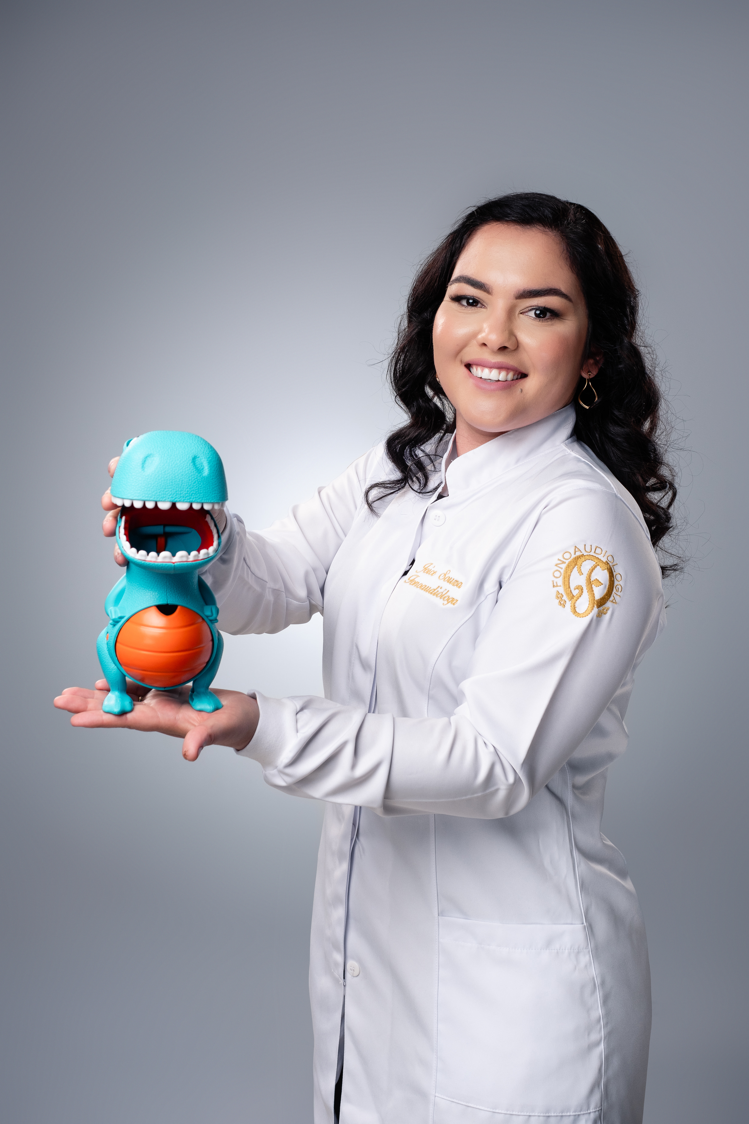 Joice Souza com jaleco segurando recurso terapêutico infantil